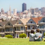 A couple sits on the lawn in front of the famous Painted Ladies houses in San Francisco, CA.